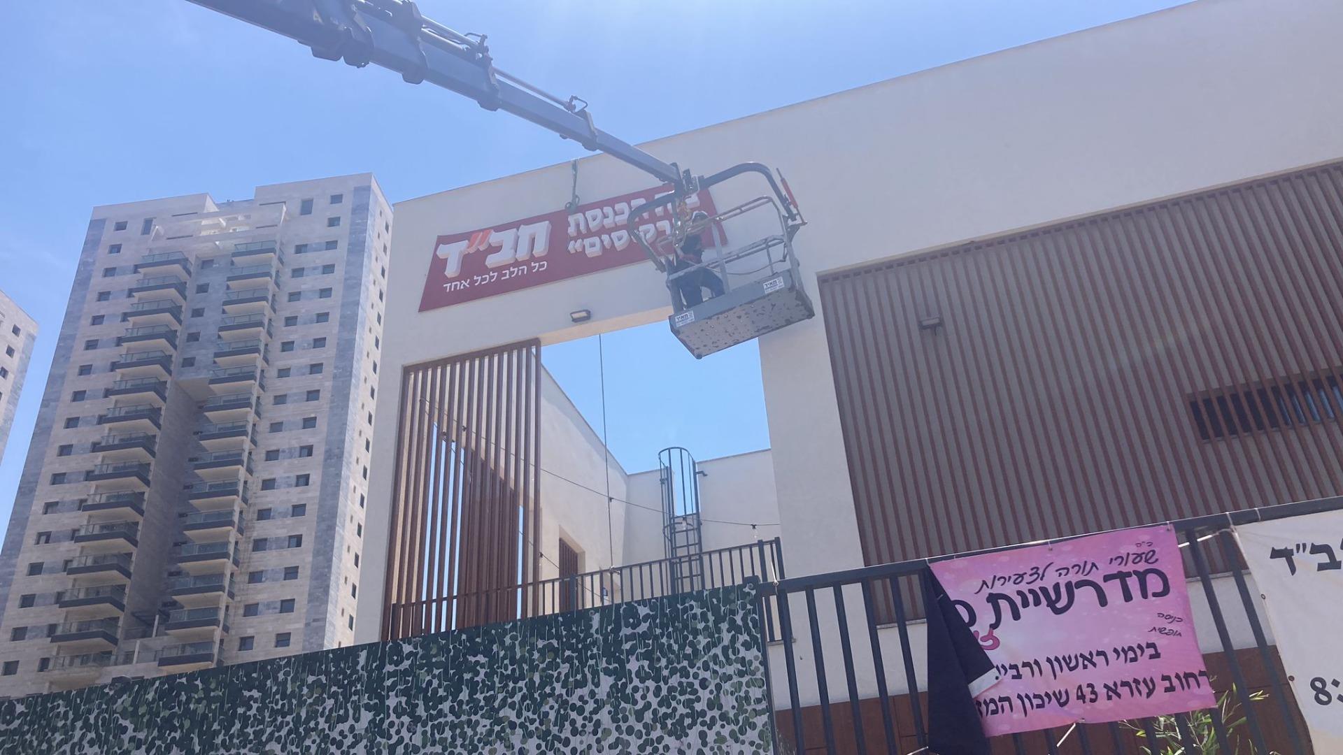סל מנוף מול שלט על בניין, ברקע מגדלים